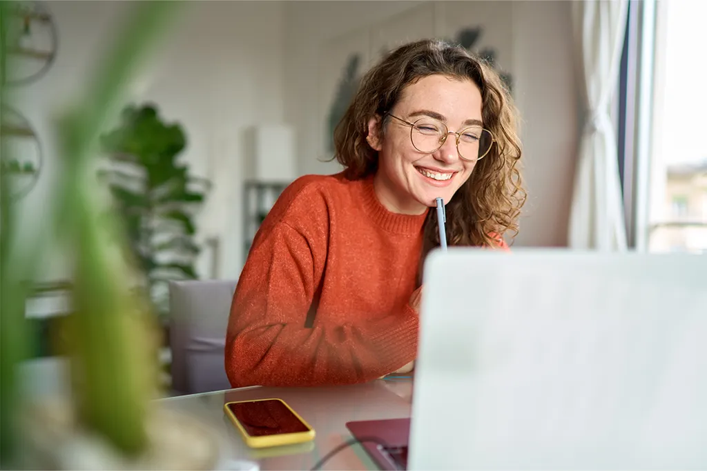 Motiviertes Arbeiten im Homeoffice Junge Frau in rotem Pullover lächelt bei der Arbeit am Laptop im Homeoffice