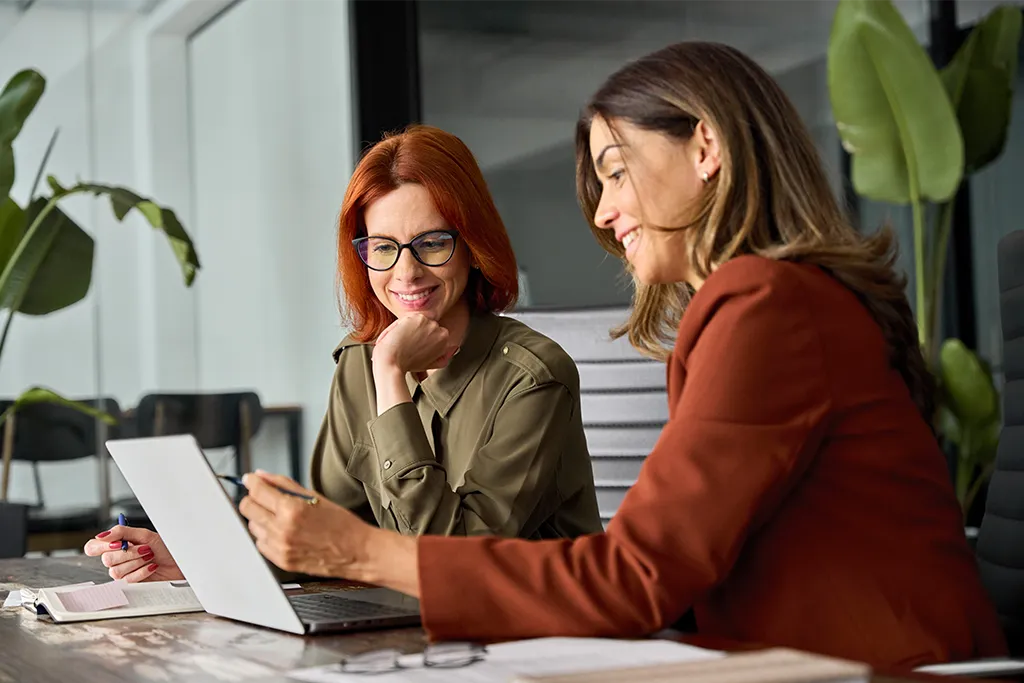 Gemeinsames Arbeiten im modernen Büro Zwei Frauen sitzen gemeinsam am Laptop und führen ein Gespräch im Büro