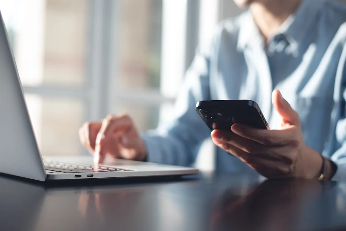 Multitasking mit Smartphone und Laptop Person nutzt gleichzeitig Smartphone und Laptop am Schreibtisch